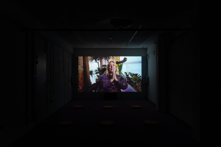 Photo from the RAPTURE exhibition, showing a dark room lit up by a screen playing the video