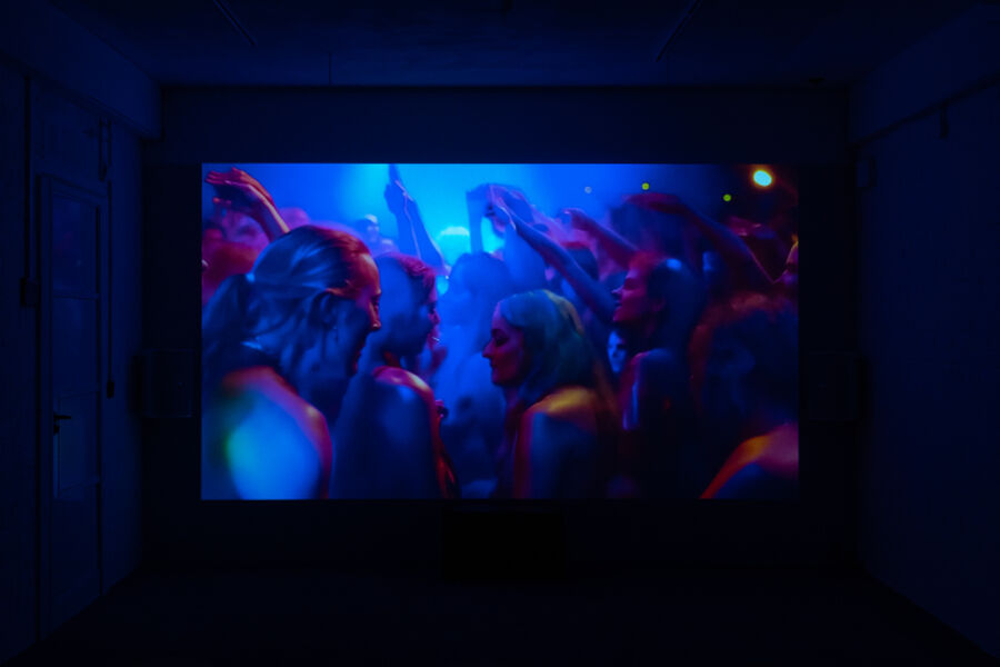 Photo from the RAPTURE exhibition, showing a dark room lit up by a screen playing the video