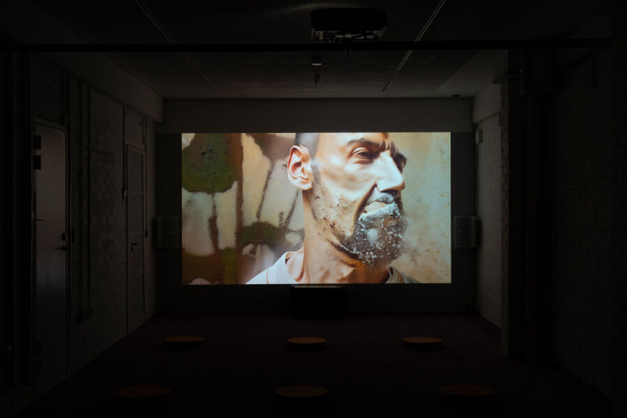 Photo from the RAPTURE exhibition, showing a dark room lit up by a screen playing the video