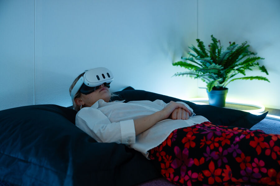 Photo from the Fields of Vision exhibition, showing a person wearing a VR headset lying down on a large cushion