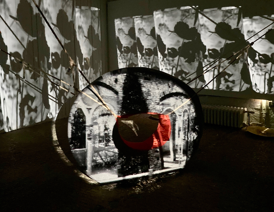Photo of an art installation in a dark room, with an object suspended by ropes and lit up by light projections
