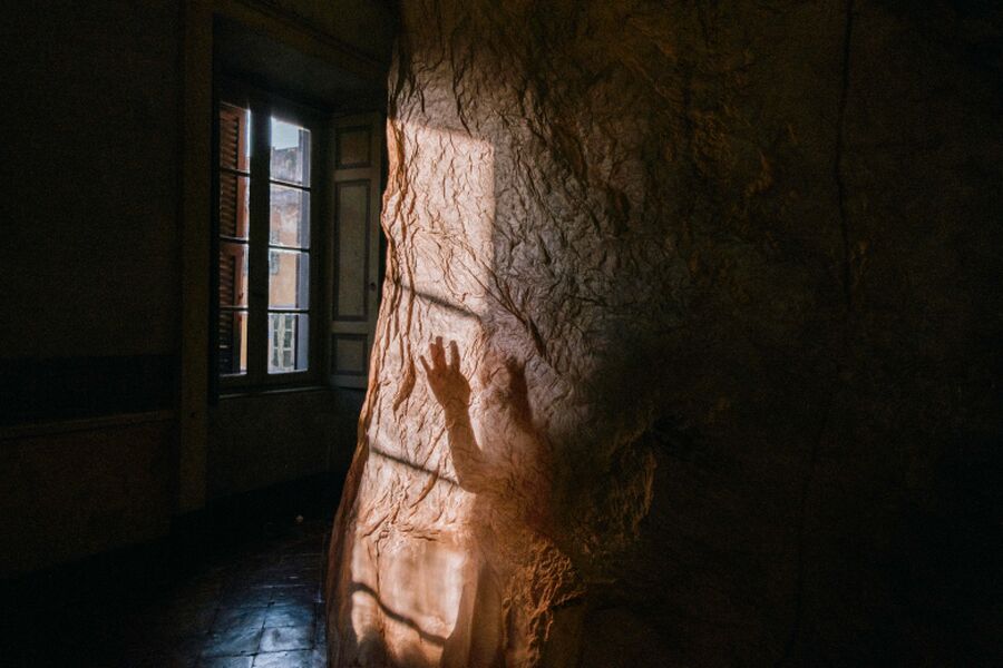 Photo of a shadow against a wall showing a person's hand reaching out in a shadowy room, by artist Fragmentario