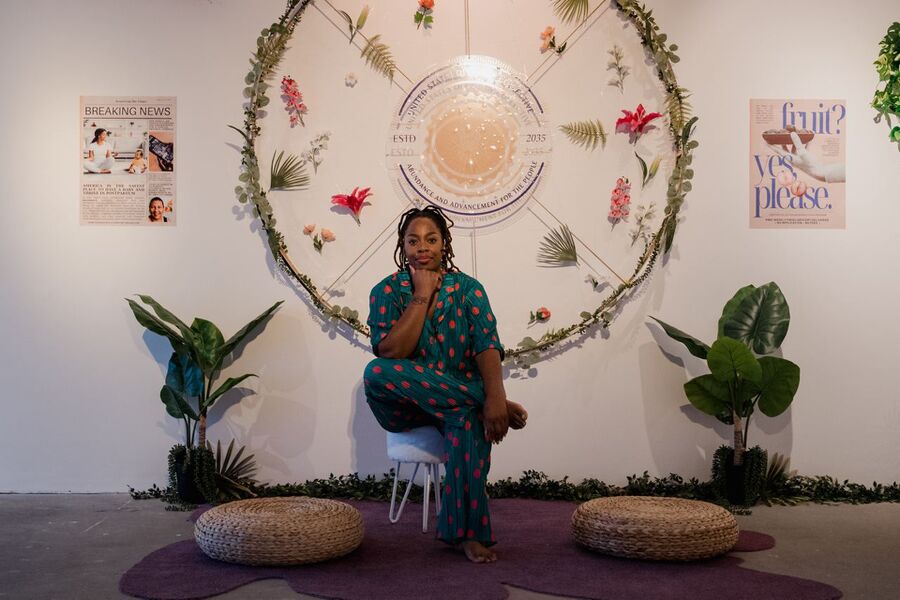 Photo of the artist Jamica El sat on a stool in amongst her installation in the Fields of Vision exhibition