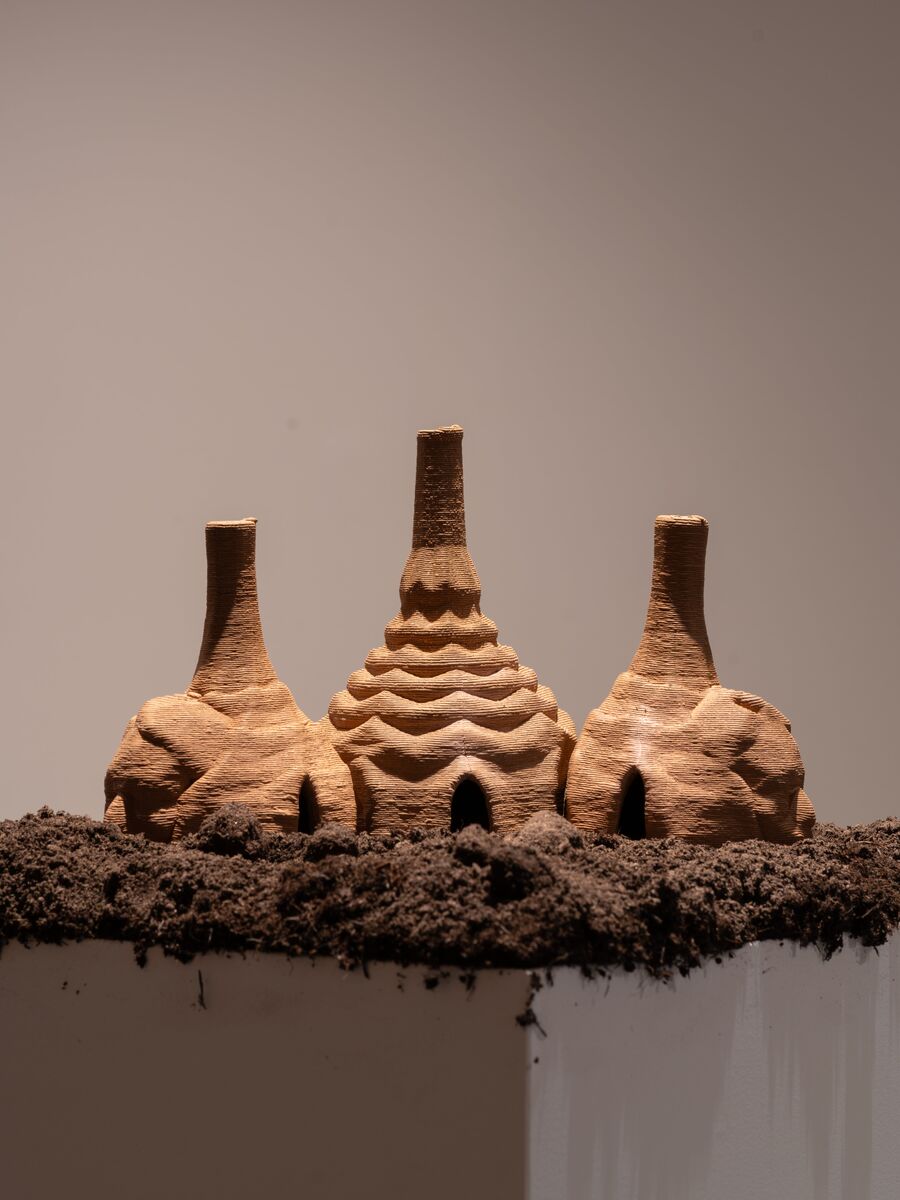Photo from the Fields of Vision exhibition, showing three clay sculptures on top of a plinth covered in soil, as part of an installation