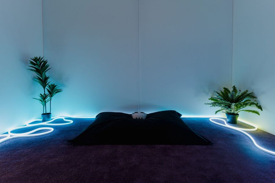 Photo from the Fields of Vision exhibition, showing a VR headset laid down on a cushion in a dark room with neon lighting